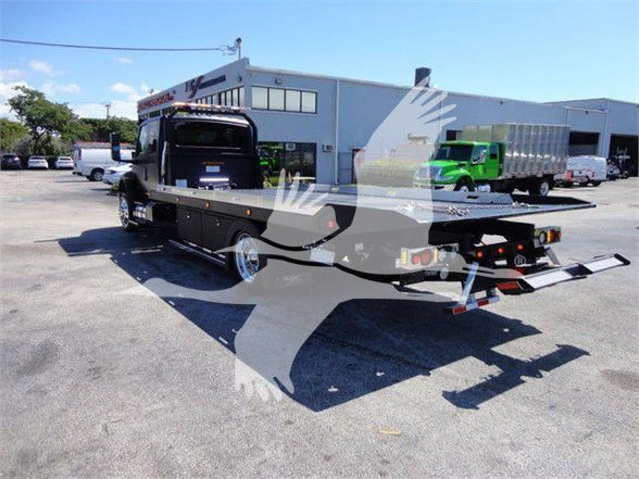 2022 International MV tow truck with flatbed in a dealership lot, black cab and flatbed, trailer ramps lowered, VIN 1HTEUMML7NH043803 visible in listing context.