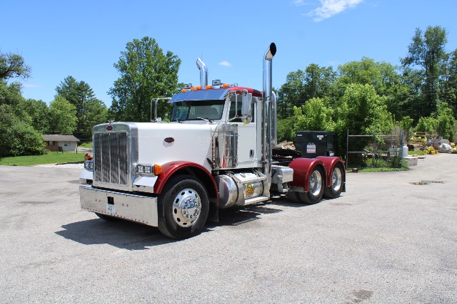 Peterbilt 379 cab and chassis truck in a gravel lot with chrome exhaust stacks and a white cab, red chassis, and chrome grille.