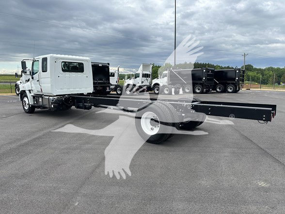 2026 Hino L6 cab and chassis with long flatbed in a parking lot, white cab, black chassis, other trucks in background.