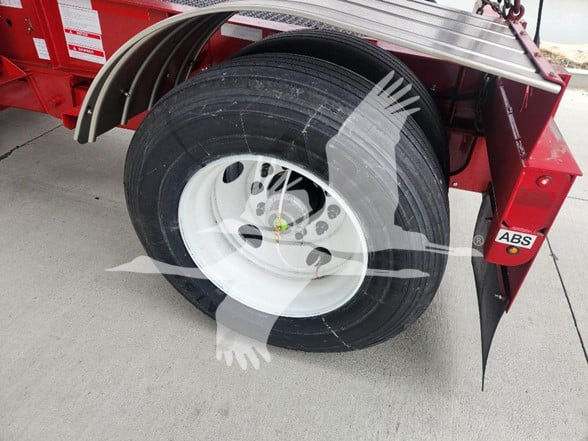 Wheel and tire assembly of a new trailer with ABS sticker, part of a red container trailer.