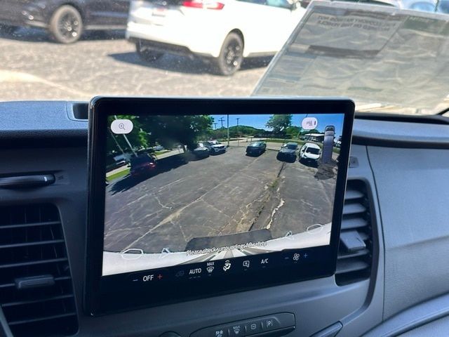 Vehicle interior infotainment display showing rear view camera feed with parked trucks and lot in background.