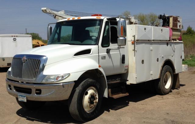 International 4300 utility truck with white cab and service body, front grille chrome, on dirt lot.