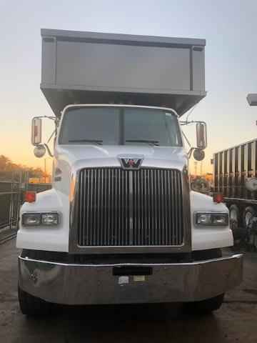 White Western Star truck with a large front grille, dual headlights, and a raised dump bed tray in the back. Front bumper is metallic and there is a badge on the grille. The truck is in an outdoor lot.