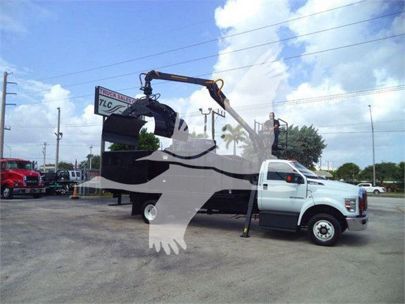 Truck with crane/grapple attachment on a white cab, displaying a large graippler arm on top and a trailer bed in a dealership lot.