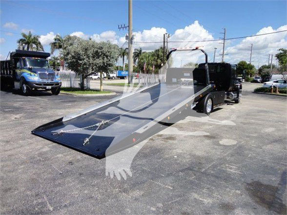 Flatbed tow truck with extended ramp in a parking lot, International MV branding and black ramp system.