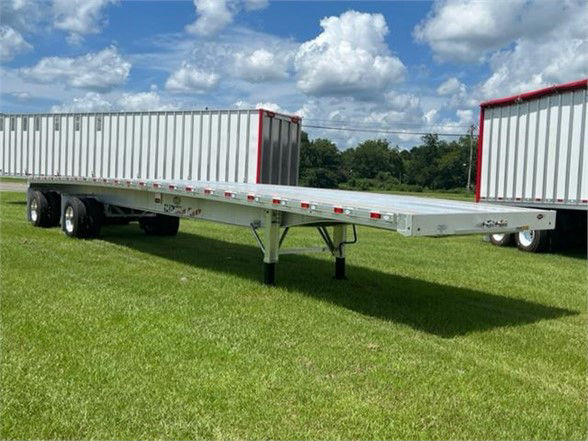 All-aluminum 48ft flatbed trailer with dual rear axles and a long flatbed section, set on grassy field under blue sky.