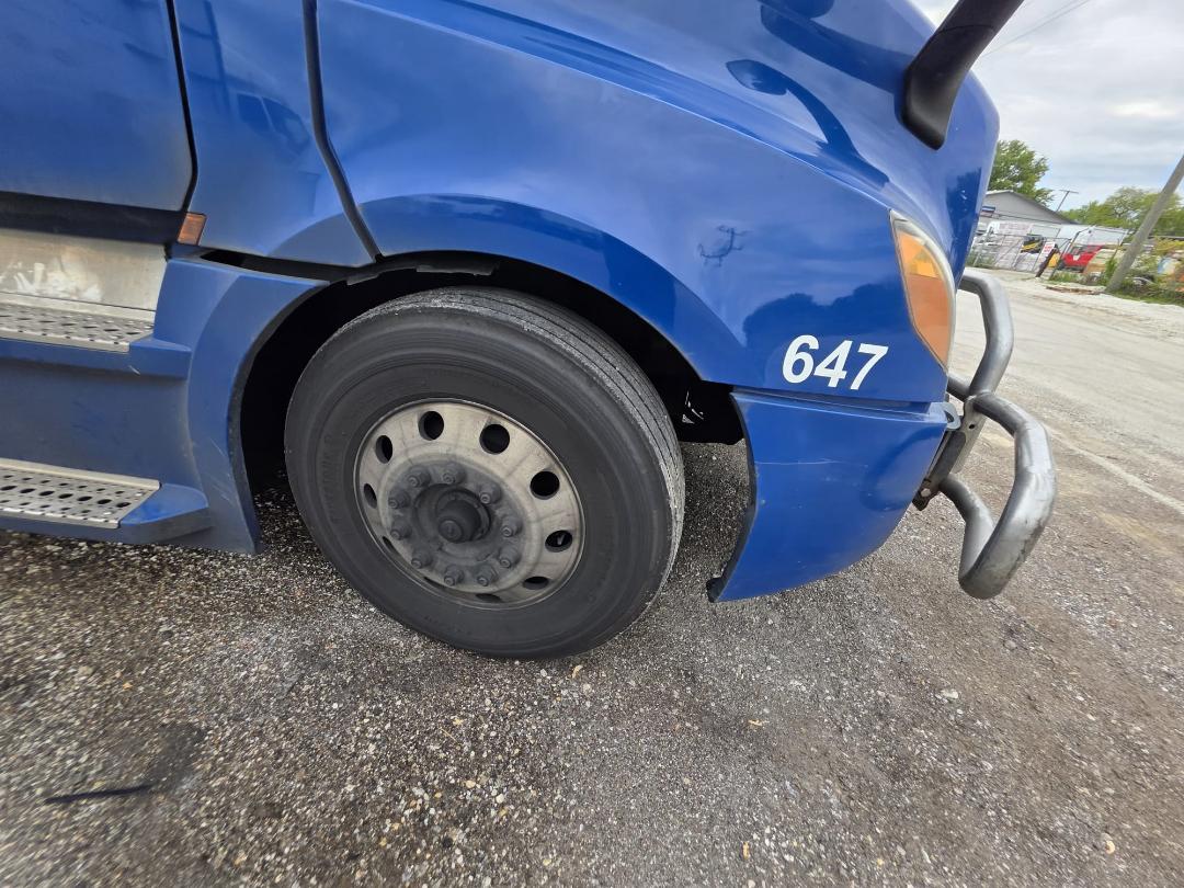 Freightliner Cascadia front wheel and bumper area with blue paint, stock number 647 decal on fender, dual bumper bars visible.