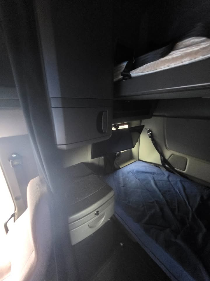 Cab interior of a 2018 International LT with sleeper bunk visible; lower storage compartment and window area; blue cover on bed.