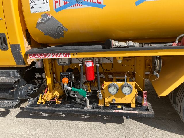 Side view of a yellow International 4200 service panel with gauges, hoses, and a red fire extinguisher mounted on a step. The label shows EMERGENCY SHUT OFF and a yellow platform with various controls.