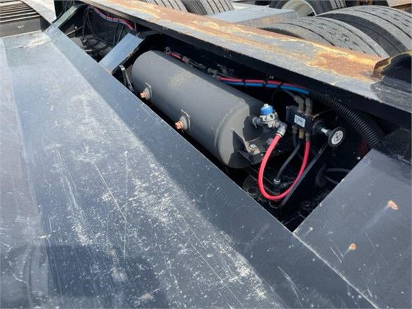 Lowboy trailer payload area with pony motor; cylindrical tank and red hoses visible in a recessed compartment on the deck edge.