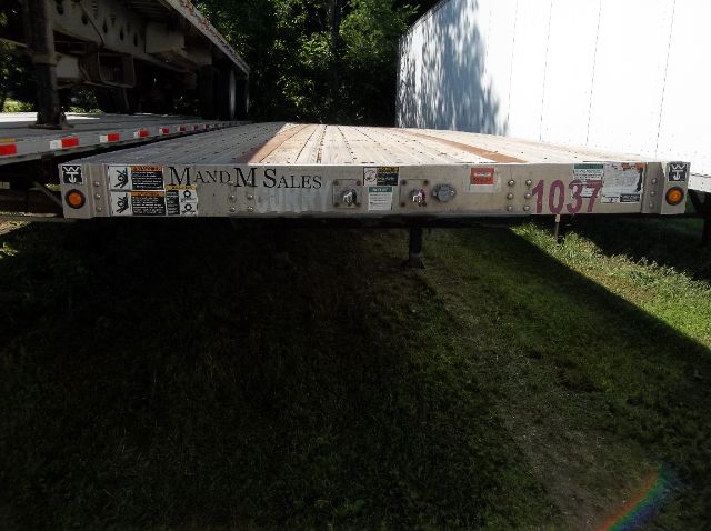 Flatbed trailer rear deck with decals and stickers showing 'MAND MSALES' and the number 1037.