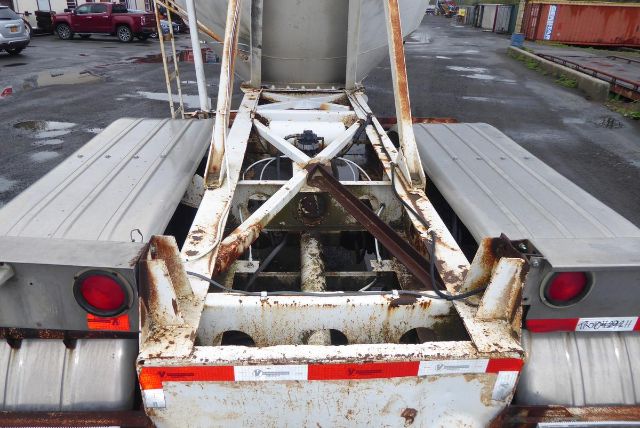 Trailer hitch area of a Fruehauf pneumatic dry bulk trailer showing rusty frame with faded white paint, rear lights, and loading hopper area.