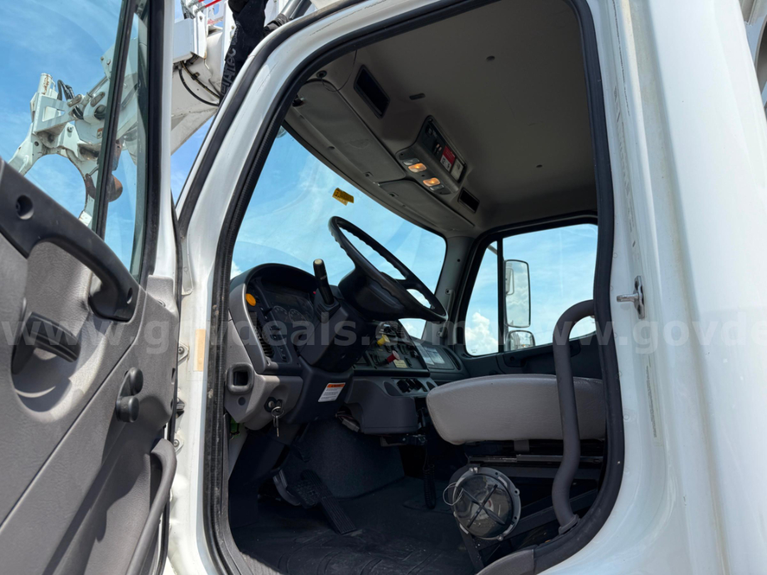 Cab interior of a Freightliner DT65 truck showing steering wheel, dashboard, and driver seat from the doorway.