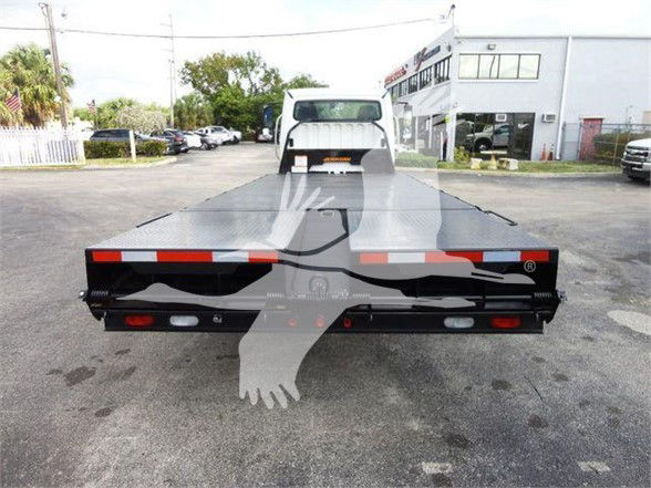 Freightliner Business Class M2 106 flatbed truck rear view showing flatbed with taillights and bumper, with dealership building in background.