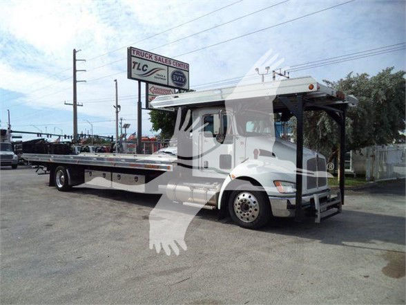Kenworth T370 tow truck with flatbed, white cab, large side mirrors, and winch area; stock number KW4CARCARRIER visible in background lot.