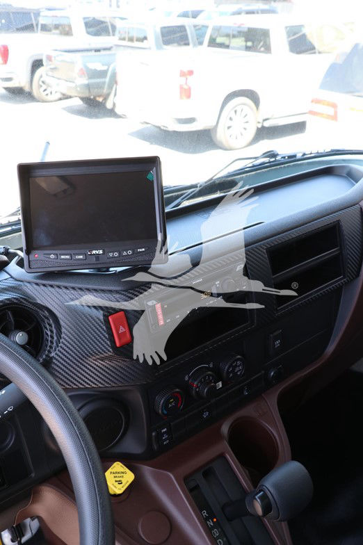 Dashboard of a 2025 Hino L6 with an aftermarket monitor mounted on the dash. Visible controls include climate dials, hazard button, and gear selector.