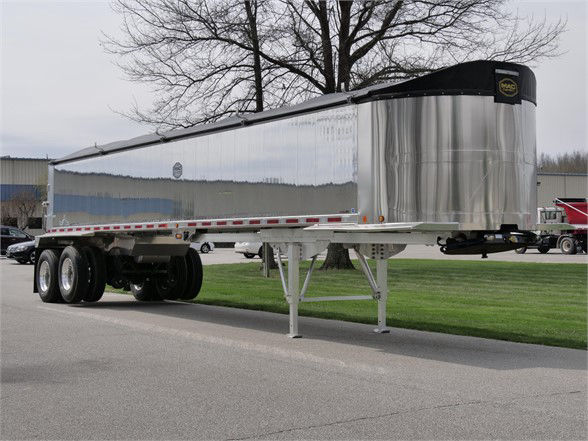 Aluminum lightweight frameless dump trailer with silver reflective sides and black tarp, three-axle setup, nose front, support legs down.