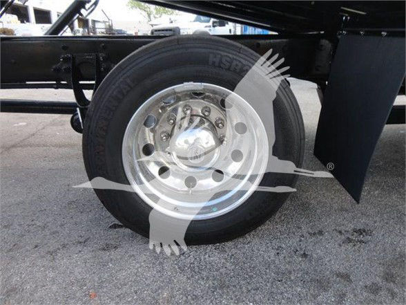 Wheel and tire assembly mounted on a truck trailer, chrome hubcap, multiple lug nuts, frame and mud flap visible.