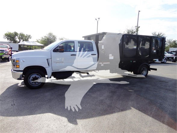 2023 Chevrolet SILVERADO 5500HD with a white cab and a black utility dump body trailer in a parking lot.
