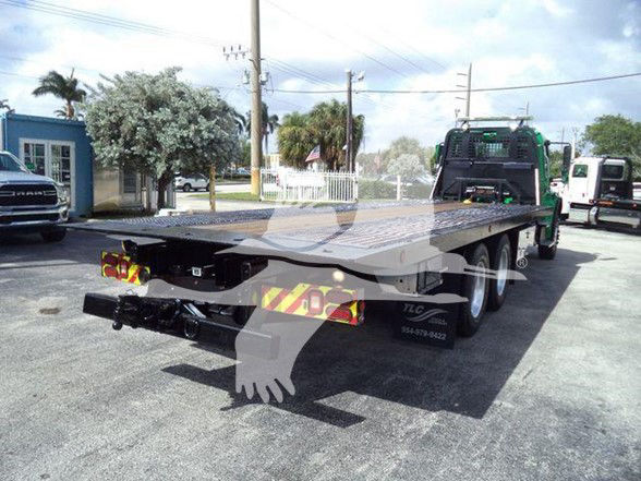 Flatbed tow truck with a long platform and twin rear axles, Freightliner BUSINESS CLASS M2 106 style chassis, rear bumper and safety reflectors visible.
