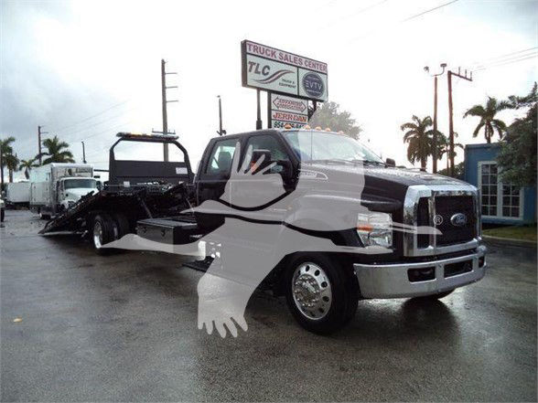 Ford F-750 tow truck in dealership lot with front chrome bumper and wheel; copy of image shows truck logo and reflection of palm trees.