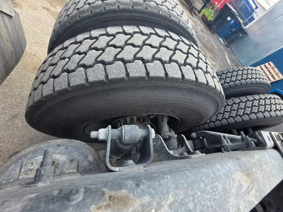 Truck part with dual tires and suspension components; visible are treaded tires and a metal hitch/connector with bolts. Some text on the tire may be present but not fully legible.