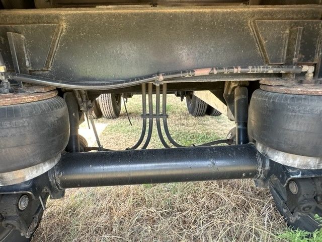Trailer undercarriage showing dual wheels on both ends, air or suspension lines, and a solid rear axle with a central driveshaft/torque tube.