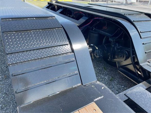 Lowboy trailer deck edge and wheel area showing diamond plate fenders and hydraulic components under a low deck.