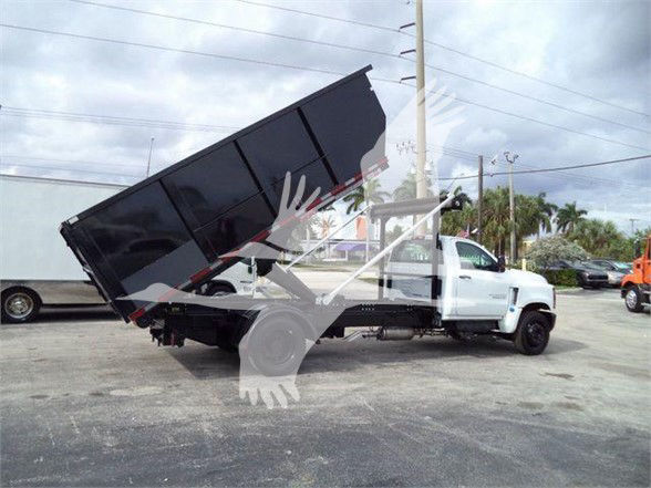 Chevrolet Silverado 6500HD dump truck in a yard with bed raised showing side view of cab and chassis.