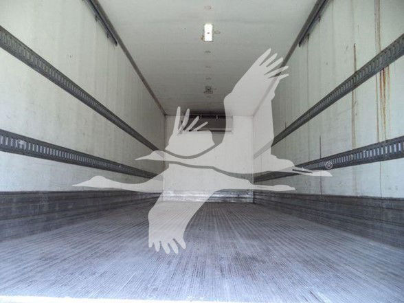 Interior of a refrigerated truck trailer cargo area with metal rails along the walls and a textured floor.