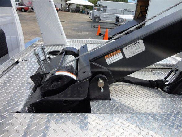 Tow equipment hitch with hydraulic winch on diamond plate platform; labels and warning stickers on the black mount, hydraulic hose, and spring mechanism.
