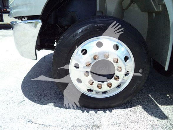 Truck front wheel and fender with chrome hub, lug nuts, and tire on a concrete surface.