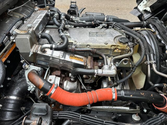 Isuzu NPR-HD engine bay showing orange radiator hose and metal engine blocks with various hoses and wires.