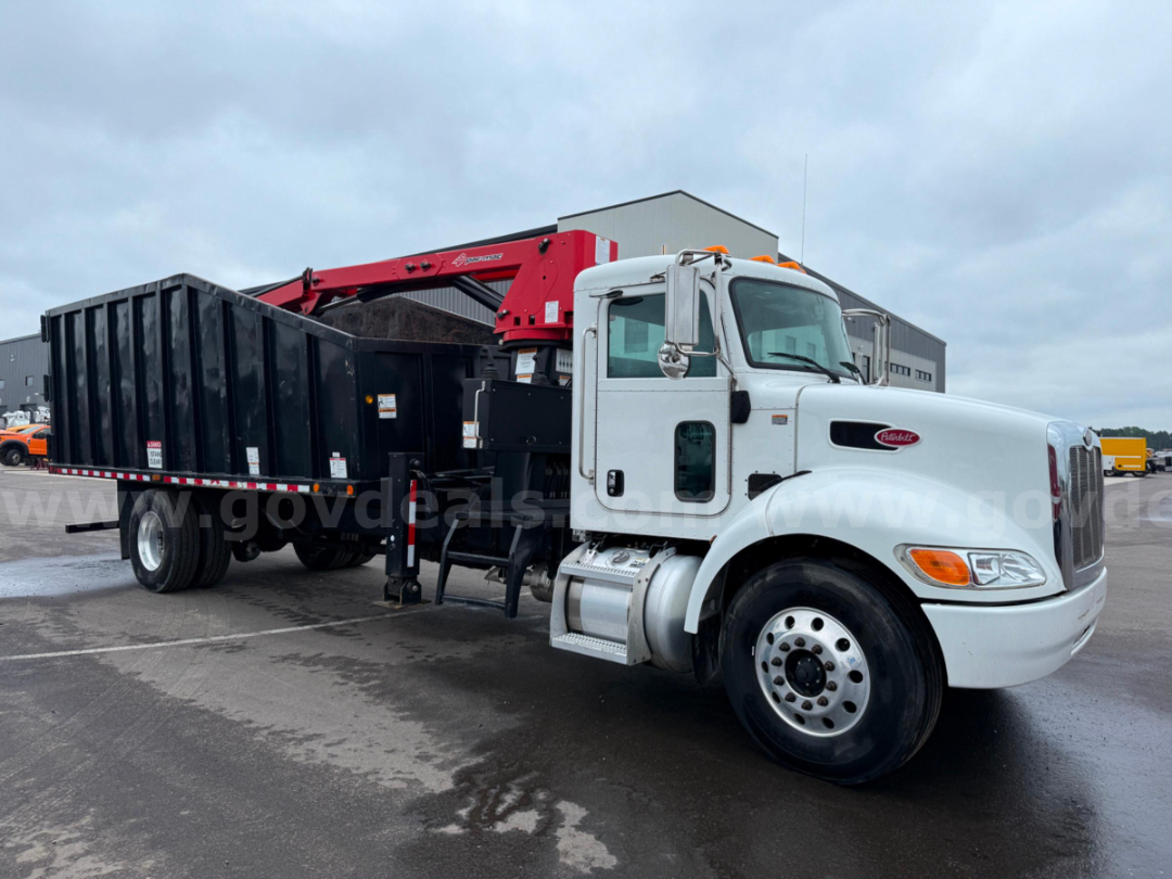 Peterbilt truck with large black dump bed and red hydraulic arm crane attachment, side view showing cab and front wheel.