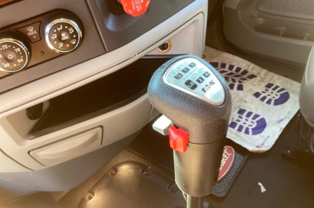 Truck interior showing gear shifter with a numbered shift pattern, climate controls on the left, and a red pull handle near center console.