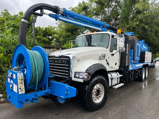 Mack GU713 vacuum truck with white cab and blue hose reel, long blue articulating arm, water vacuum unit on chassis, identifiable labels on equipment and hoses.