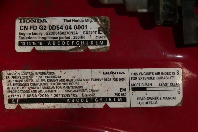 Label sticker with Honda engine information and emissions data on a red surface, showing engine family G20D54S0270N2A GX270T-EM1 and various compliance text.