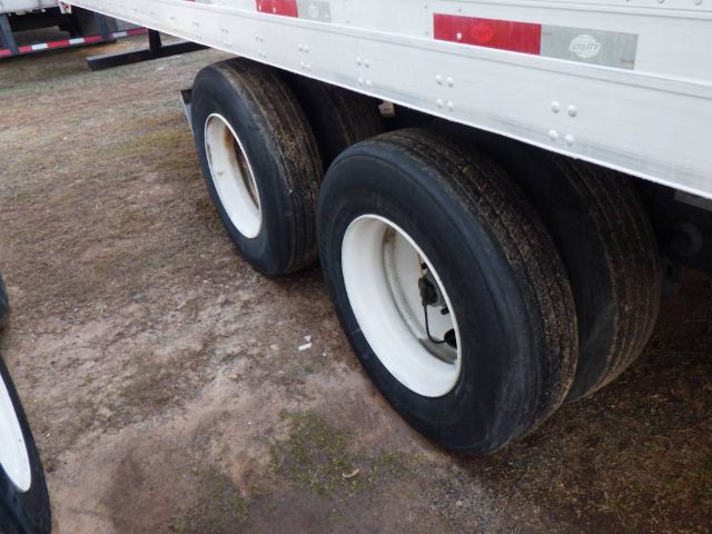 Dual rear wheels of a trailer with white rims and black tires under a silver trailer side, dirt ground visible.