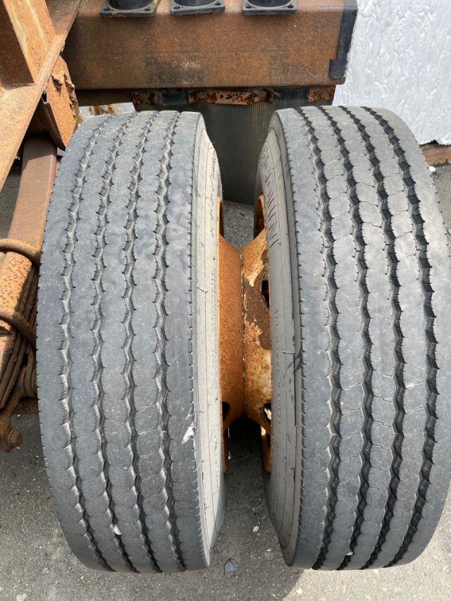 Dual rear truck wheels showing worn tread on both tires with rusted orange wheel hubs and suspension components visible between.