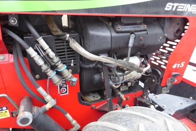 Tractor engine bay showing hydraulic hoses, fittings, and engine components on a Steiner 415 in-service agricultural equipment.