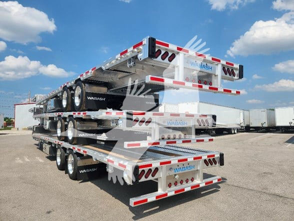 New Wabash drop deck trailer stacked on a multi-axle flatbed with white and red reflective stripes, Wabash logos on sides and ends.