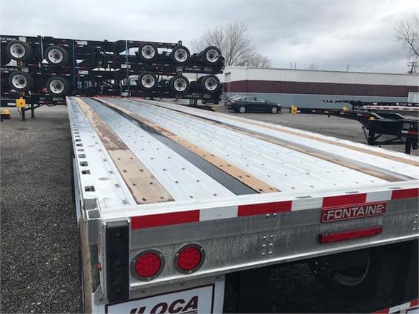 Flatbed trailer bed with wooden planks and metal rails, Fontaine label on rear, stacked trailers in background.