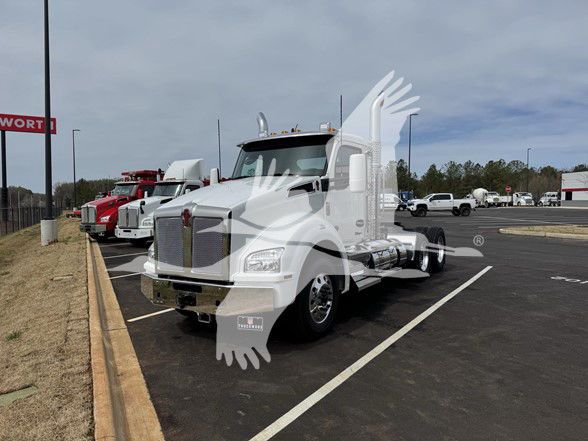 Kenworth T880 conventional daycab truck in a dealership lot, white cab, chrome grille, parked in marked space with other trucks in background.