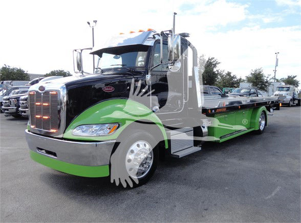 2022 Peterbilt 337 tow truck with black cab and green lower body, chrome grille, and flatbed. Visible text on truck includes Peterbilt badge on grille.