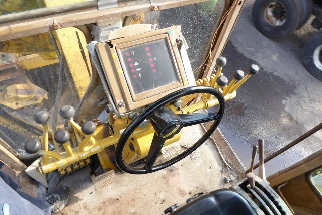 Caterpillar 16G engine room with steering wheel and control panel, various levers, and a digital display mounted on yellow metal frame.