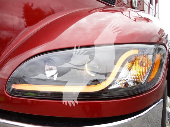 Headlight area of a red 2022 Peterbilt 337 truck with a distinctive orange daytime running light and chrome trim.