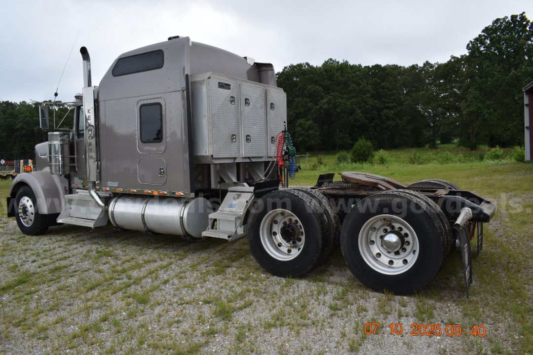 Kenworth W900 cab and chassis truck side view with sleeper cab, aluminum toolbox, and dual rear axles showing chrome fuel tanks and chassis hardware.