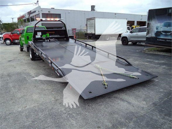 Truck tow truck with a flatbed trailer and loading ramps, parked in a lot.