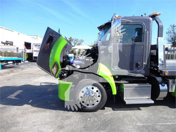 2022 Peterbilt 337 side view showing the hood raised, green accents, chrome wheels, and steps near the cab.
