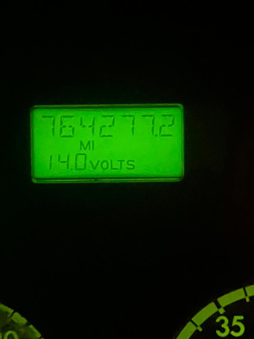 Glowing green digital display showing mileage 764277.2 mi and 14.0 volts in dashboard context.